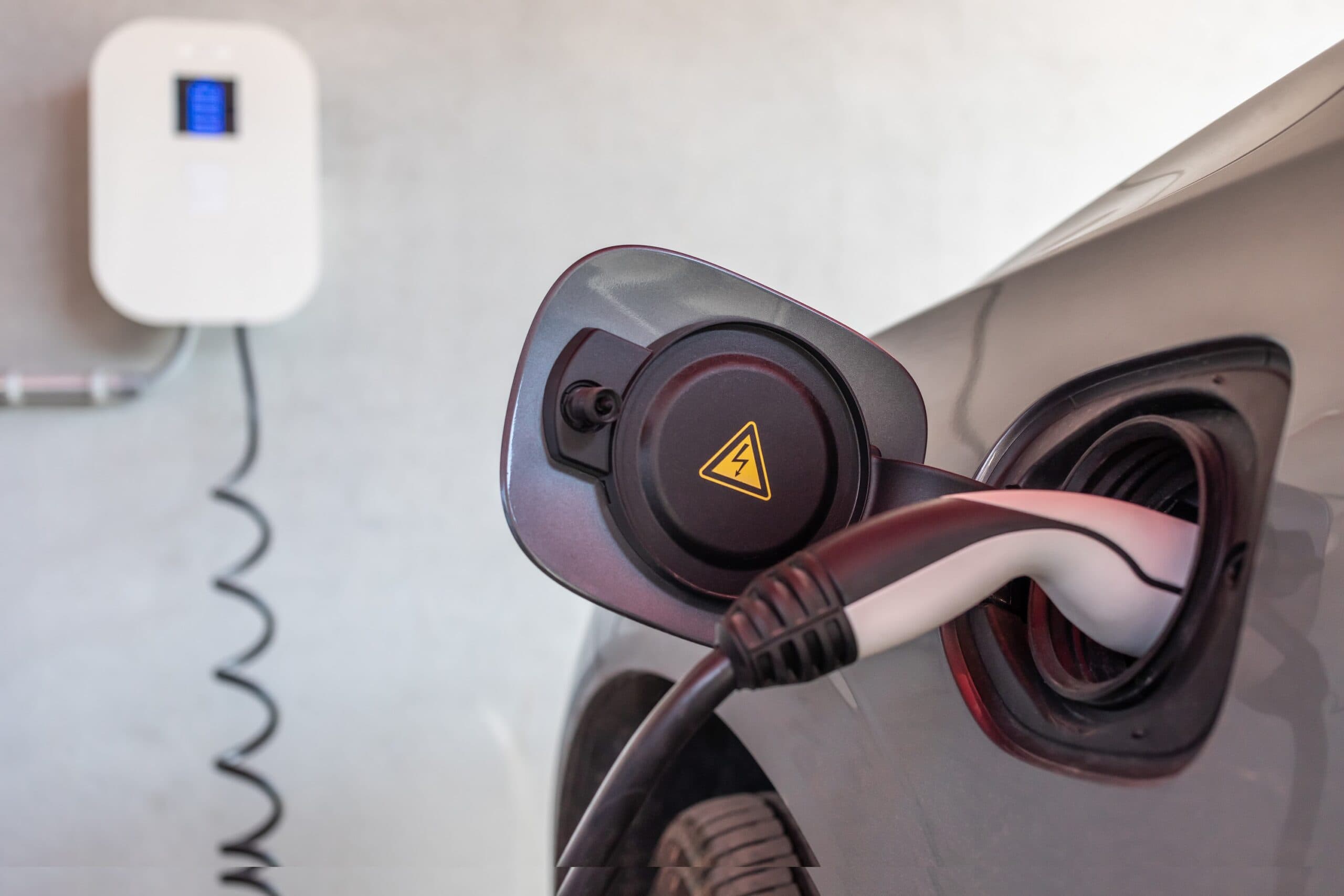 EV charging cable plugged into a car with a wall-mounted charger unit in the background